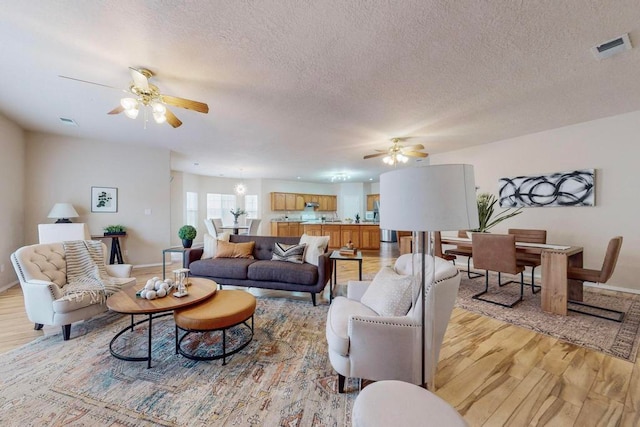 living room with ceiling fan, a textured ceiling, and light hardwood / wood-style flooring