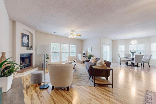 living room featuring a textured ceiling, a wealth of natural light, light hardwood / wood-style flooring, and ceiling fan with notable chandelier