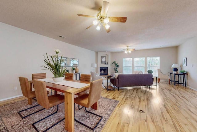 dining space with ceiling fan, a fireplace, a textured ceiling, and light wood-type flooring