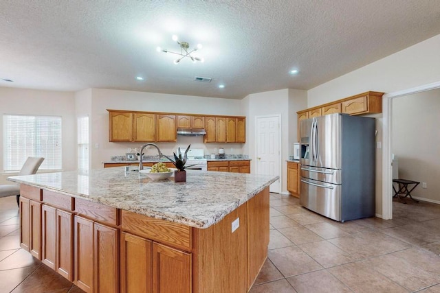 kitchen featuring stainless steel fridge, sink, light tile patterned floors, and an island with sink