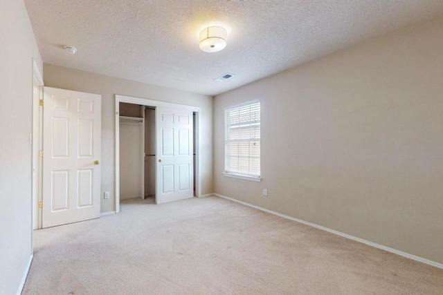 unfurnished bedroom with a textured ceiling, light carpet, and a closet