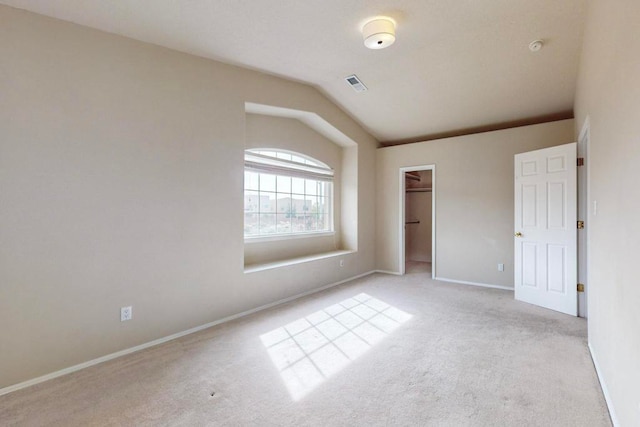 unfurnished bedroom with light carpet, a closet, vaulted ceiling, and a spacious closet