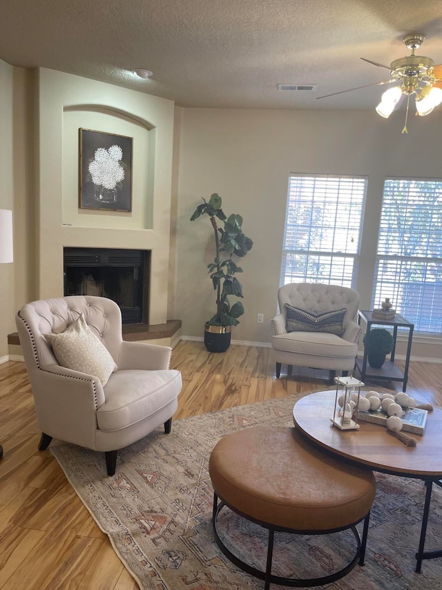 living room featuring ceiling fan, light wood-type flooring, and a textured ceiling