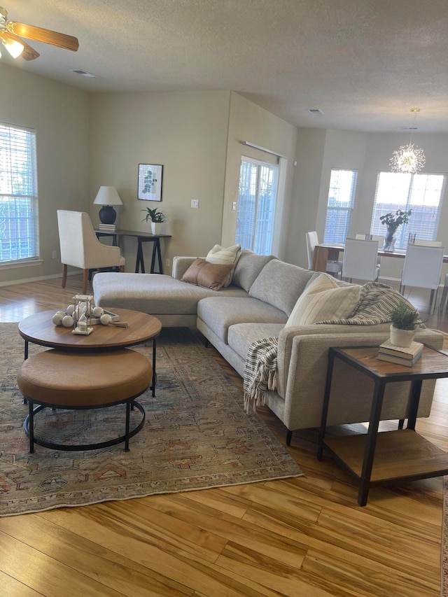 living room with ceiling fan with notable chandelier, a textured ceiling, and light wood-type flooring