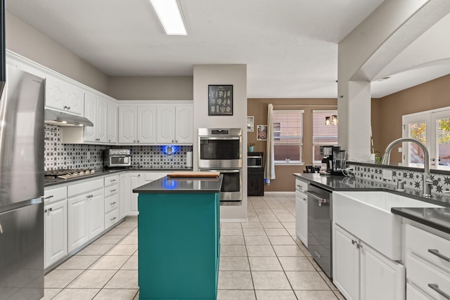 kitchen featuring sink, light tile patterned floors, appliances with stainless steel finishes, a center island, and white cabinets