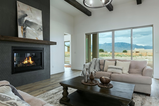 living room featuring beam ceiling, a mountain view, a towering ceiling, wood-type flooring, and a tiled fireplace