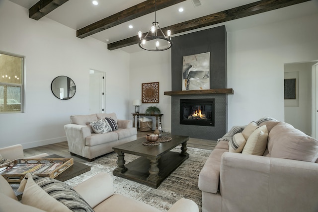 living room with beam ceiling, a large fireplace, an inviting chandelier, and light hardwood / wood-style flooring