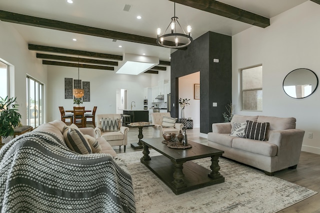 living room with a skylight, beamed ceiling, a towering ceiling, a chandelier, and wood-type flooring