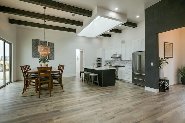 dining room featuring a skylight, sink, a high ceiling, light hardwood / wood-style flooring, and beamed ceiling