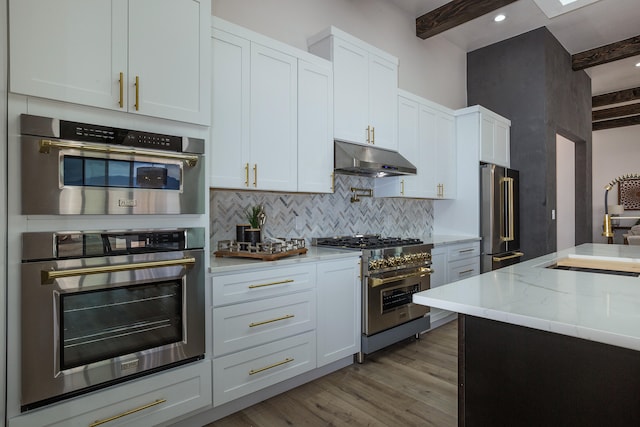 kitchen with white cabinets, beam ceiling, premium appliances, and light hardwood / wood-style floors