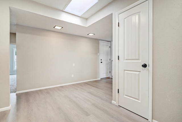 unfurnished room featuring a skylight and light hardwood / wood-style flooring