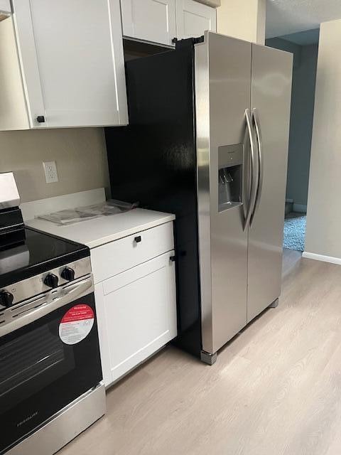 kitchen with light hardwood / wood-style flooring, white cabinets, and stainless steel appliances