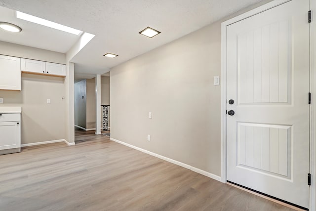 interior space featuring white cabinets, light hardwood / wood-style floors, and a textured ceiling