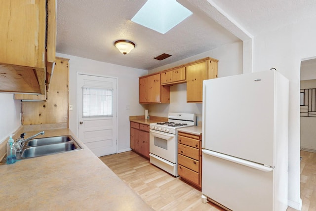 kitchen with a textured ceiling, a skylight, sink, white appliances, and light hardwood / wood-style flooring