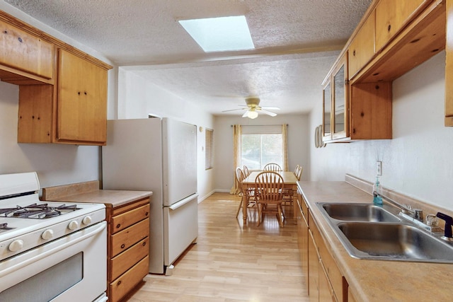 kitchen featuring sink, ceiling fan, a skylight, white appliances, and light wood-type flooring