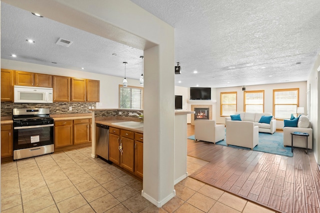 kitchen with sink, stainless steel appliances, a textured ceiling, decorative backsplash, and light tile patterned floors