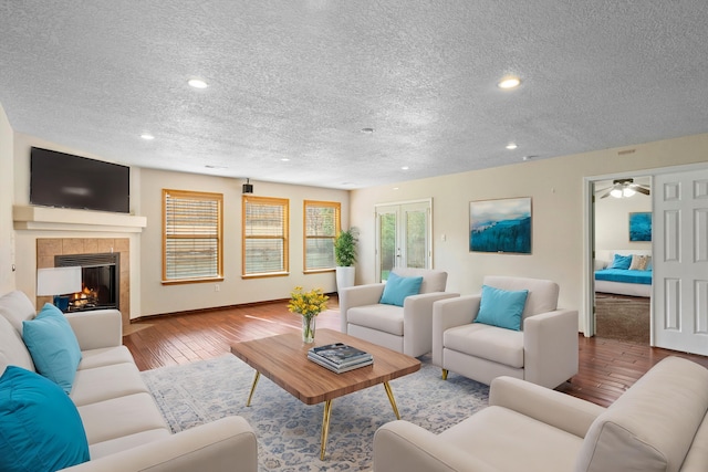 living room featuring ceiling fan, french doors, light hardwood / wood-style floors, a textured ceiling, and a fireplace