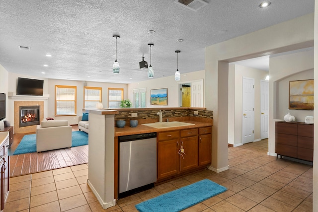 kitchen with a tile fireplace, sink, stainless steel dishwasher, decorative light fixtures, and light tile patterned flooring