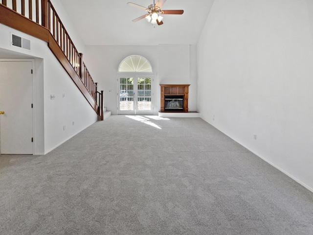 unfurnished living room with ceiling fan, light carpet, a high ceiling, and french doors