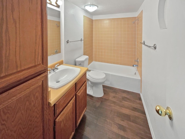 full bathroom with vanity, hardwood / wood-style flooring, tiled shower / bath combo, toilet, and a textured ceiling