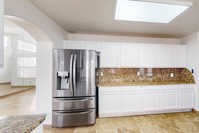 kitchen featuring white cabinetry, stainless steel fridge, backsplash, and dark stone counters