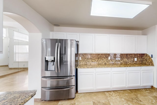 kitchen featuring white cabinets, stainless steel fridge, backsplash, and dark stone counters