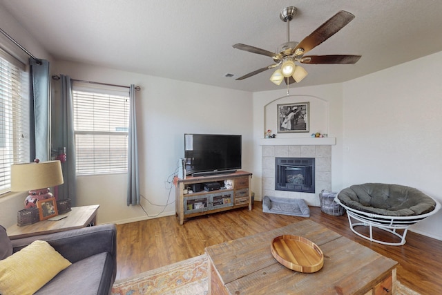 living room with hardwood / wood-style flooring, ceiling fan, and a tiled fireplace