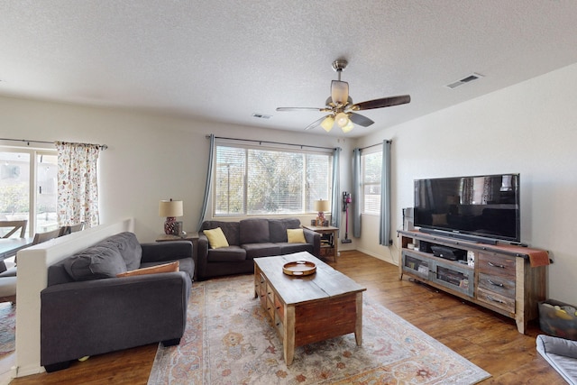 living room featuring wood-type flooring, ceiling fan, and a textured ceiling