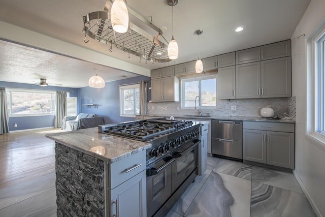 kitchen with open floor plan, light stone countertops, stainless steel dishwasher, double oven range, and a sink