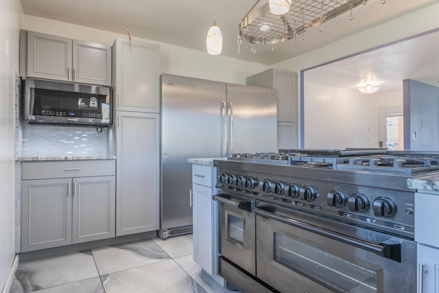 kitchen featuring hanging light fixtures, gray cabinets, stainless steel appliances, backsplash, and light tile patterned flooring