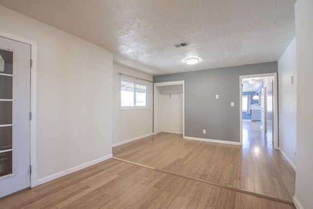 unfurnished room featuring visible vents, light wood-style flooring, baseboards, and a textured ceiling