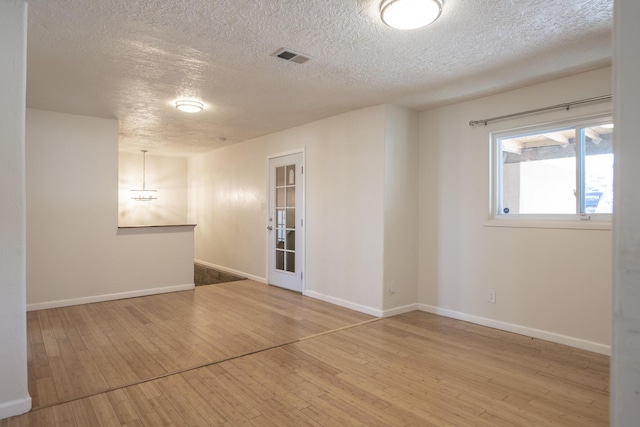 unfurnished room featuring visible vents, a textured ceiling, baseboards, and wood finished floors