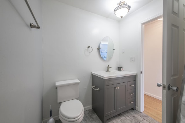 half bath with toilet, baseboards, wood finished floors, and vanity