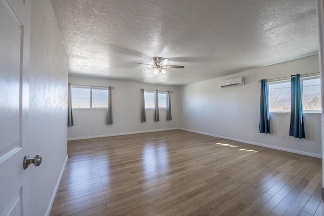 empty room featuring a wall unit AC, ceiling fan, a textured ceiling, wood finished floors, and baseboards