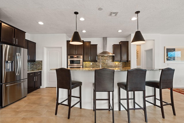 kitchen with an island with sink, pendant lighting, wall chimney exhaust hood, and stainless steel appliances