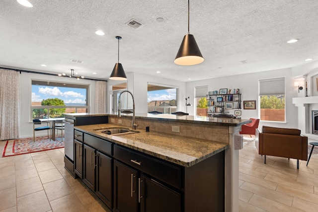 kitchen featuring a center island with sink, decorative light fixtures, light stone counters, and sink