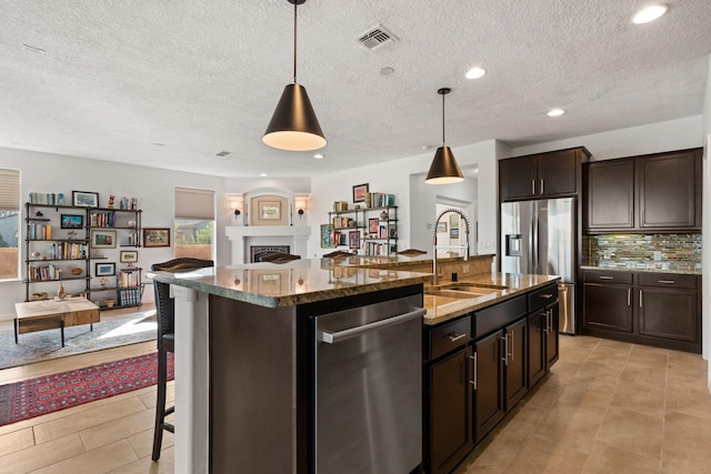 kitchen featuring dark brown cabinets, stainless steel appliances, sink, hanging light fixtures, and an island with sink