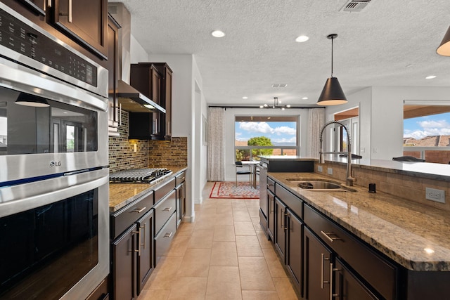 kitchen with decorative backsplash, appliances with stainless steel finishes, light stone counters, sink, and pendant lighting