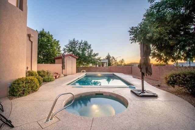 pool at dusk featuring a shed and an in ground hot tub