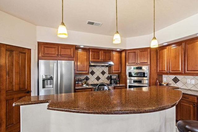 kitchen featuring tasteful backsplash, a center island with sink, hanging light fixtures, and appliances with stainless steel finishes