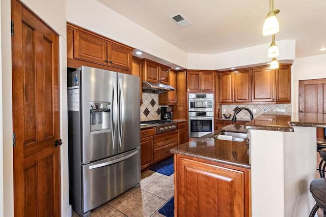 kitchen featuring sink, dark stone countertops, an island with sink, appliances with stainless steel finishes, and a kitchen bar