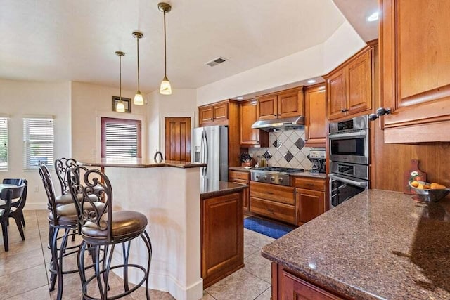 kitchen with dark stone counters, pendant lighting, a kitchen bar, a kitchen island, and appliances with stainless steel finishes