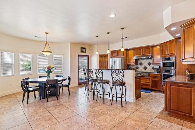 kitchen with stainless steel appliances, light tile patterned floors, a kitchen breakfast bar, pendant lighting, and a kitchen island