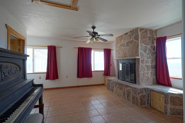 unfurnished living room with light tile patterned floors, a stone fireplace, ceiling fan, and a healthy amount of sunlight