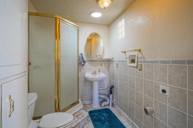 bathroom with a textured ceiling, toilet, an enclosed shower, and tile walls