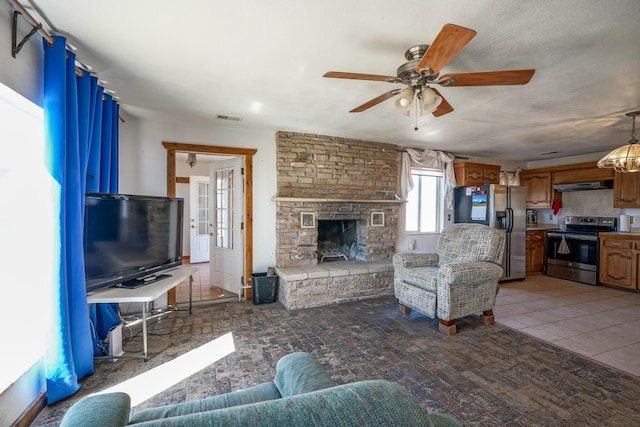 living room featuring ceiling fan, a fireplace, and a textured ceiling