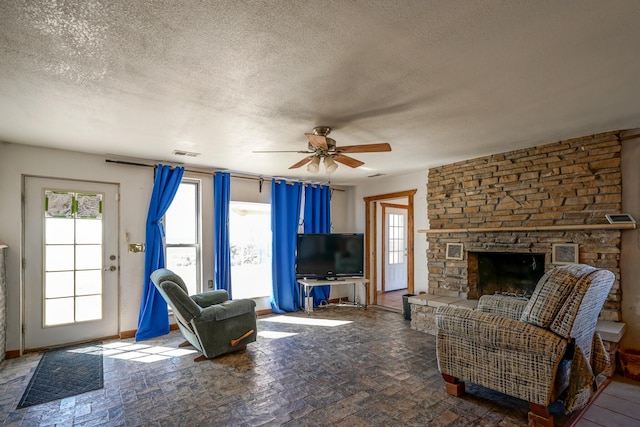 living room featuring ceiling fan, a fireplace, and a textured ceiling