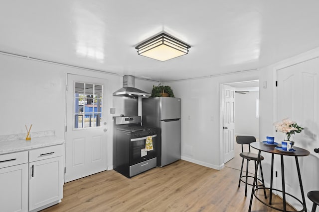 kitchen featuring light stone countertops, stainless steel appliances, wall chimney range hood, white cabinets, and light wood-type flooring