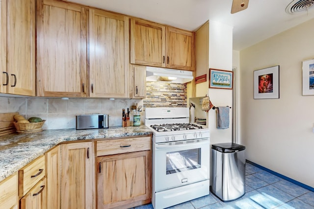 kitchen featuring white gas range, light tile patterned floors, light brown cabinetry, and decorative backsplash