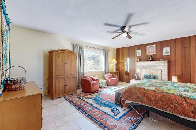 bedroom with a brick fireplace, ceiling fan, a textured ceiling, and wood walls